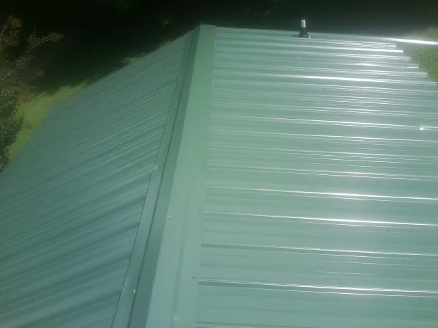 New green metal panels meeting at the ridge of a roof — Flat Roof Repair work by our crew in Oakville